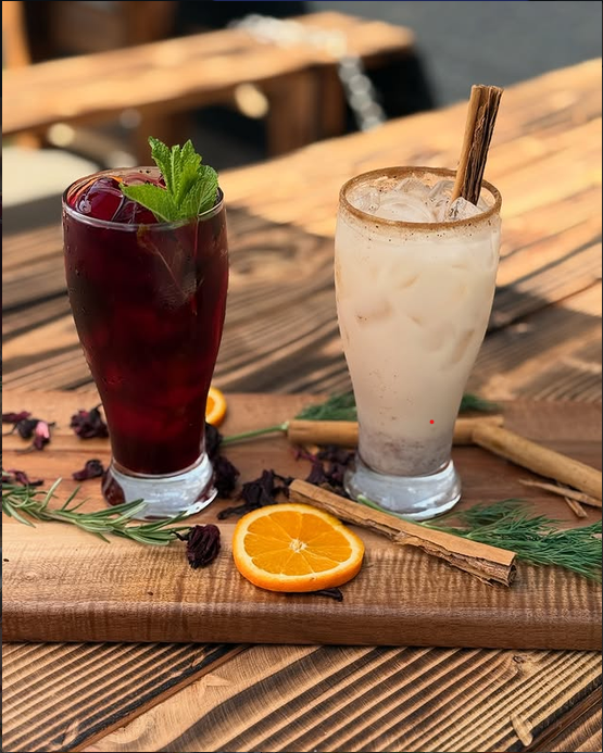 Agua de jamaica y horchata en vasos altos sobre una tabla de madera con canela, naranja y flor de jamaica