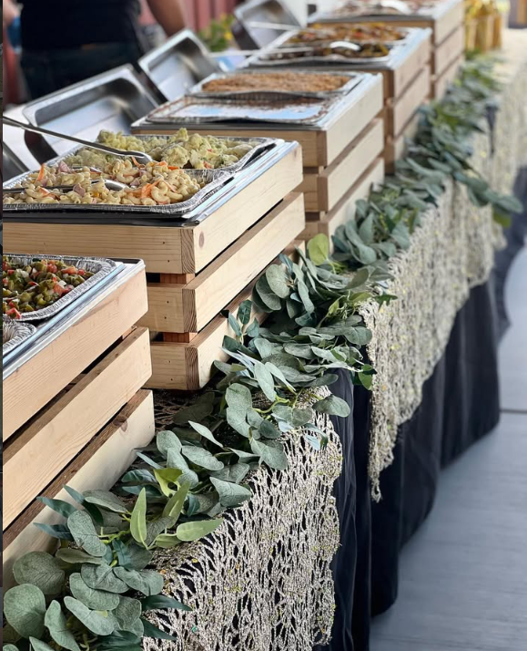 Línea de buffet montada sobre cajas de madera con mantelería negra