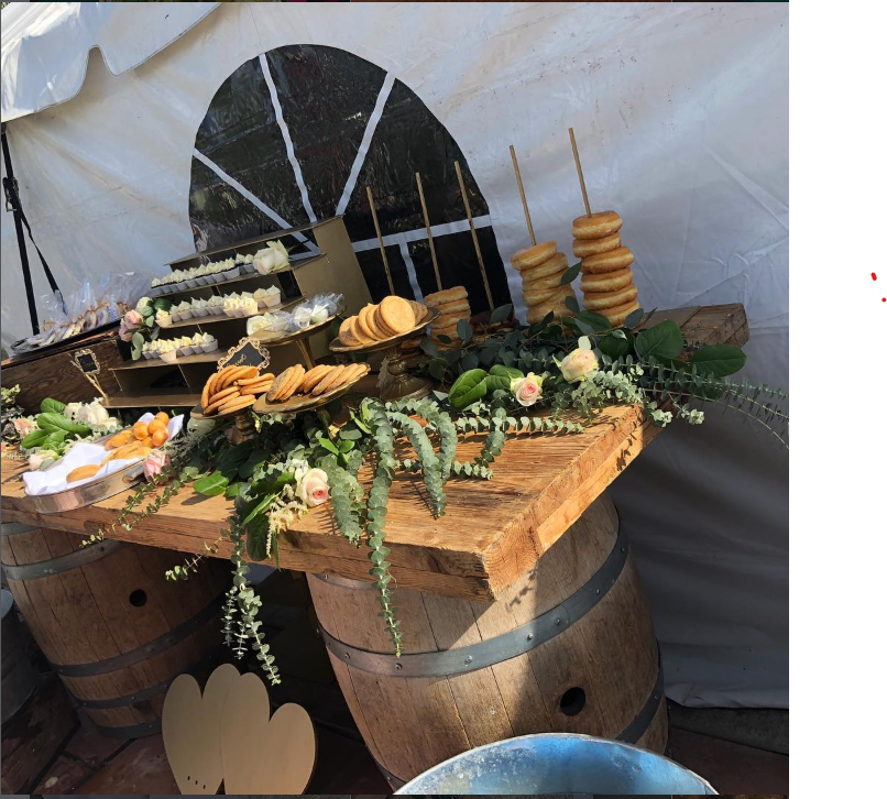 Mesa de postres montada sobre barricas de vino, decorada con eucalipto y rosas