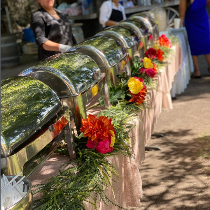 Buffet al aire libre con mantel rosado y arreglos florales de colores