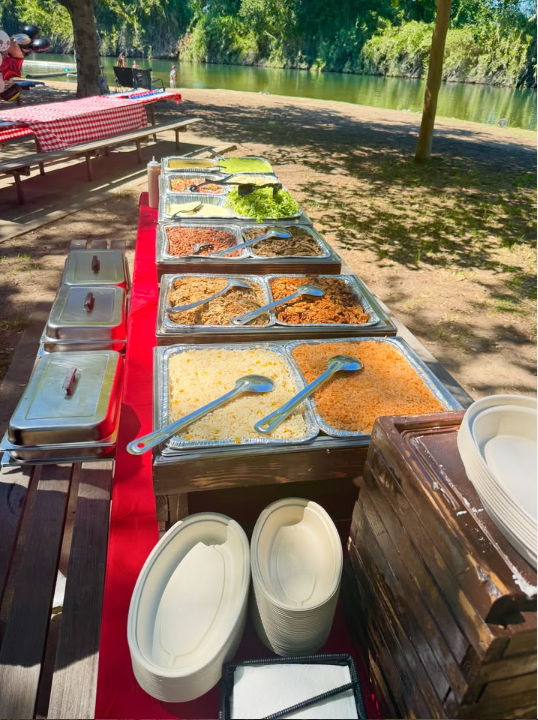 Buffet al aire libre junto al río con mesas de picnic y mantel rojo