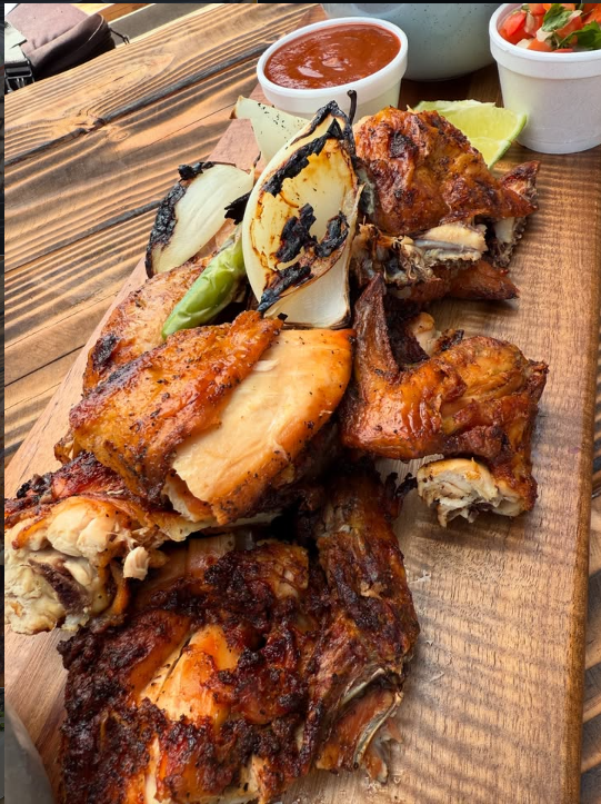 Pollo asado a la parrilla en tabla de madera con cebollitas, limón, salsa y pico de gallo