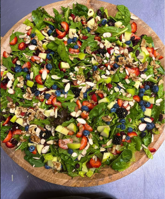 Ensalada de espinaca con fresa, mora azul, manzana verde, nuez y almendra en un tazón grande de madera